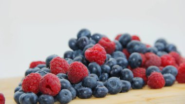 Beyaz arka planda taze ahududu ve yaban mersini. Yaban mersini ve ahududu ağaçtan bir arka planda.