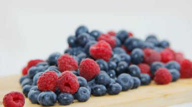 Beyaz arka planda taze ahududu ve yaban mersini. Yaban mersini ve ahududu ağaçtan bir arka planda.