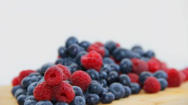 Beyaz arka planda taze ahududu ve yaban mersini. Yaban mersini ve ahududu ağaçtan bir arka planda.