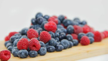 Beyaz arka planda taze ahududu ve yaban mersini. Yaban mersini ve ahududu ağaçtan bir arka planda.