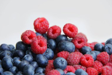 Beyaz arka planda taze ahududu ve yaban mersini. Yaban mersini ve ahududu ağaçtan bir arka planda.