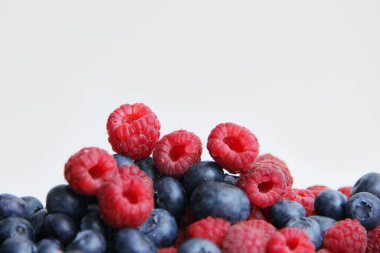 Beyaz arka planda taze ahududu ve yaban mersini. Yaban mersini ve ahududu ağaçtan bir arka planda.