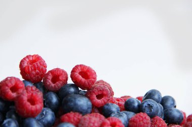 Beyaz arka planda taze ahududu ve yaban mersini. Yaban mersini ve ahududu ağaçtan bir arka planda.