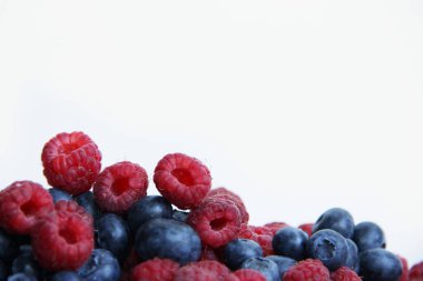 Beyaz arka planda taze ahududu ve yaban mersini. Yaban mersini ve ahududu ağaçtan bir arka planda.