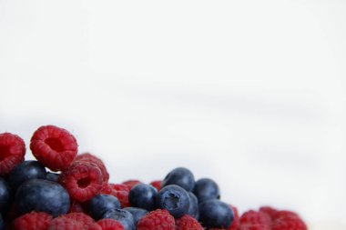 Beyaz arka planda taze ahududu ve yaban mersini. Yaban mersini ve ahududu ağaçtan bir arka planda.