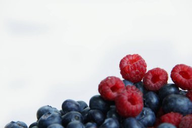 Beyaz arka planda taze ahududu ve yaban mersini. Yaban mersini ve ahududu ağaçtan bir arka planda.