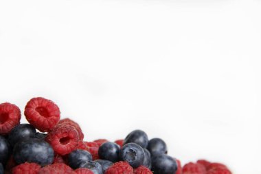 Beyaz arka planda taze ahududu ve yaban mersini. Yaban mersini ve ahududu ağaçtan bir arka planda.