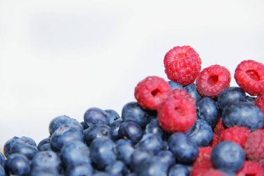 Beyaz arka planda taze ahududu ve yaban mersini. Yaban mersini ve ahududu ağaçtan bir arka planda.