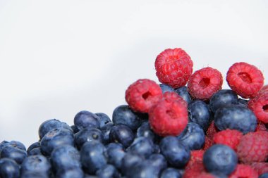 Beyaz arka planda taze ahududu ve yaban mersini. Yaban mersini ve ahududu ağaçtan bir arka planda.