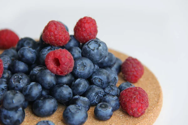 Beyaz arka planda taze ahududu ve yaban mersini. Yaban mersini ve ahududu ağaçtan bir arka planda.