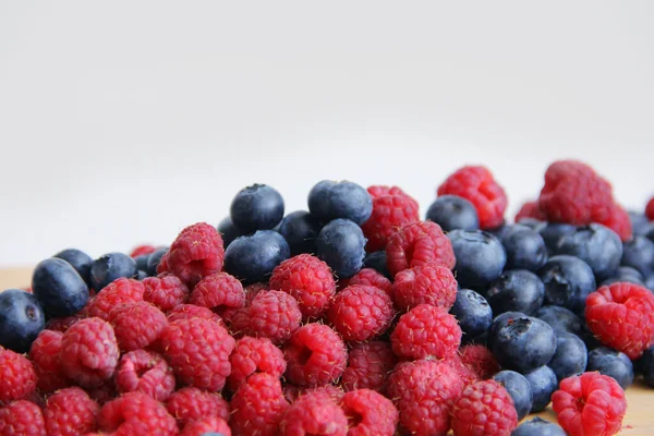 Fresh raspberries and blueberries on a white background close-up. wild summer berries blueberries and raspberries on a wooden background