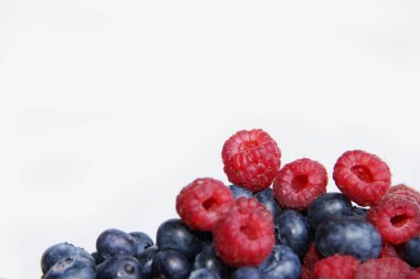 Beyaz arka planda taze ahududu ve yaban mersini. Yaban mersini ve ahududu ağaçtan bir arka planda.