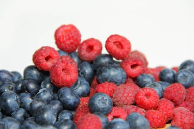 Beyaz arka planda taze ahududu ve yaban mersini. Yaban mersini ve ahududu ağaçtan bir arka planda.