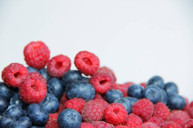 Beyaz arka planda taze ahududu ve yaban mersini. Yaban mersini ve ahududu ağaçtan bir arka planda.