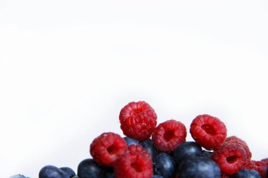 Beyaz arka planda taze ahududu ve yaban mersini. Yaban mersini ve ahududu ağaçtan bir arka planda.