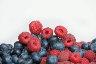 Beyaz arka planda taze ahududu ve yaban mersini. Yaban mersini ve ahududu ağaçtan bir arka planda.