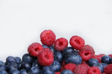 Beyaz arka planda taze ahududu ve yaban mersini. Yaban mersini ve ahududu ağaçtan bir arka planda.