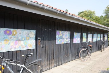 Okul bahçesinde duvarında sanat eserleri olan bir bisiklet kulübesi.