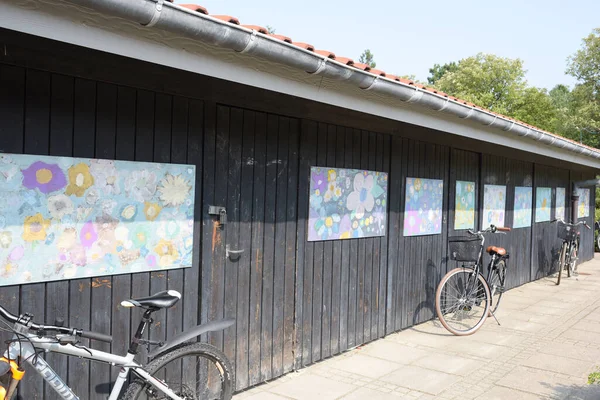 Okul bahçesinde duvarında sanat eserleri olan bir bisiklet kulübesi.