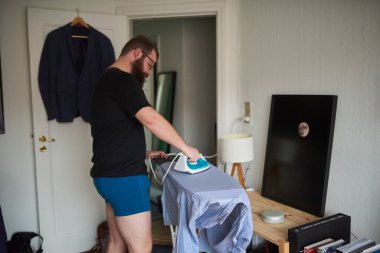 Adam dairesinde ev işleri yapıyor ve gömleğini ütülüyor.