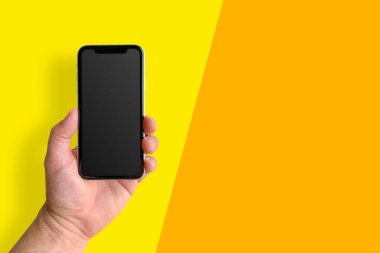 Sarı ve turuncu arka planda boş ekranlı cep telefonu tutan adam, yakın plan. Metin için boşluk