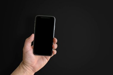 Elinde cep telefonu olan bir adam siyah arka planda boş ekranlı, eli yakın. Metin için boşluk