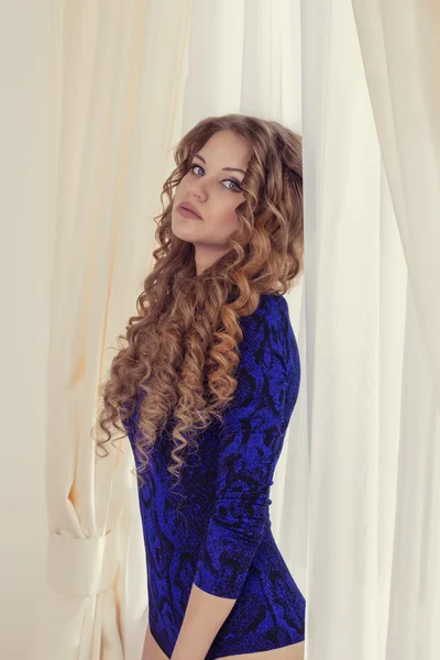 Elegant woman with curly hair at the curtains