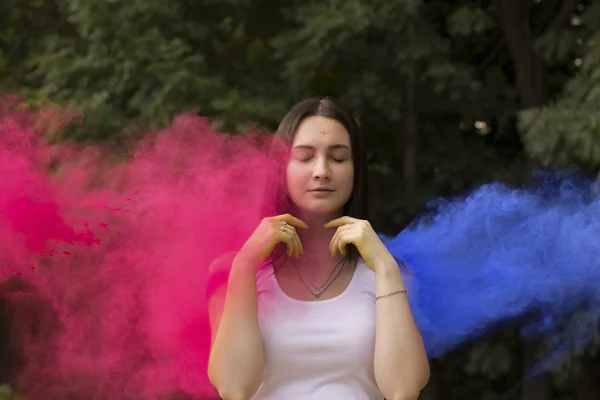 Beautiful woman with colorful powder blowing in her face — Stock Photo, Image