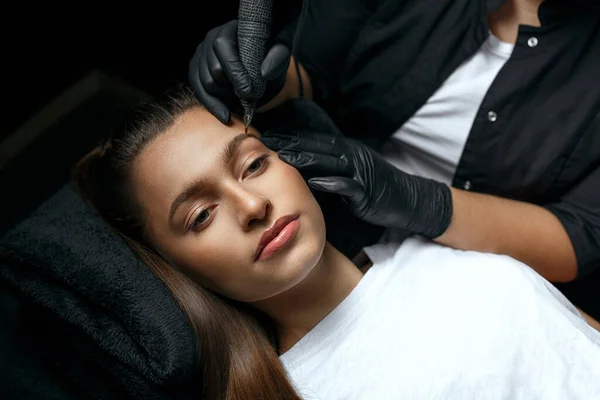 Beauty master applying eyebrows permanent makeup at the beauty salon. Closeup shot