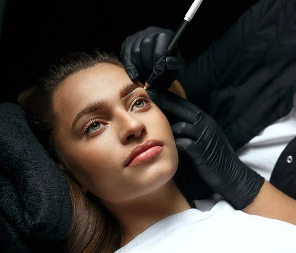 Brow stylist making eyebrows shape with white pencil before permanent makeup procedure