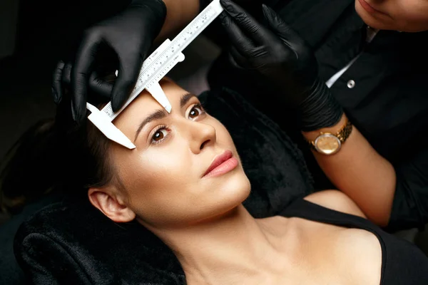 Beauty master measuring eyebrows with calipers before powder permanent makeup. Closeup shot