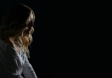 Kıvırcık saçlı zarif sarışın bir kadının dramatik portresi beyaz gömlek giyer. Derin gölgelerle çekilen stüdyo çekimi. Boş boşluk