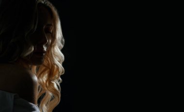 Dalgalı saçlı, duygusal sarışın bir kadının dramatik yakın plan portresi beyaz gömlek giyer. Derin gölgelerle çekilen stüdyo çekimi. Metin için boşluk