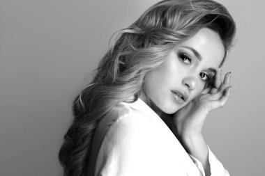 Uzun kıvırcık saçlı muhteşem sarışın kadın şık beyaz ceket giyiyor. Siyah beyaz portre