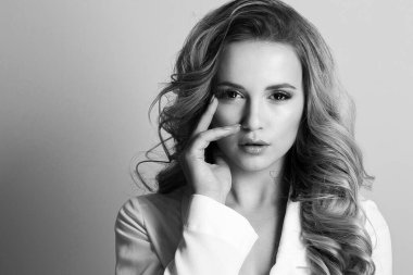 Uzun kıvırcık saçlı çekici sarışın kadın şık beyaz ceket giyiyor. Boşluk. Siyah beyaz portre