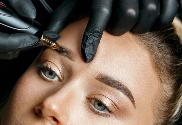 Cosmetician doing eyebrow tattooing on a female brows. Closeup sho