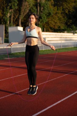 Muhteşem esmer kadın stadyumdaki antrenman sırasında atlama ipiyle spor giysileri giyer.