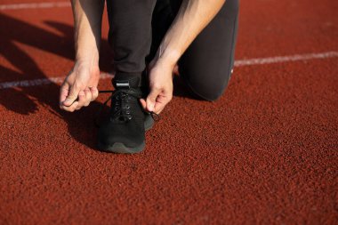 Genç koşucu koşu pistinde ayakkabı bağcıkları bağlıyor. Yakın çekim.