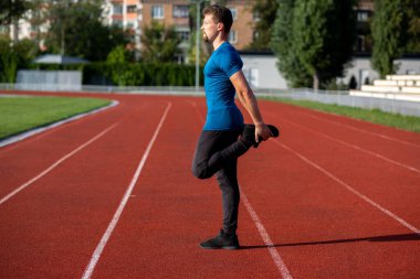 Genç atletik adam koşudan önce koşu pistinde esneme hareketleri yapıyor. Metin için boşluk