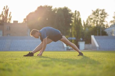 Stadyumda koşmadan önce güçlü sakallı adam bacak esnetiyor. Boş alan  