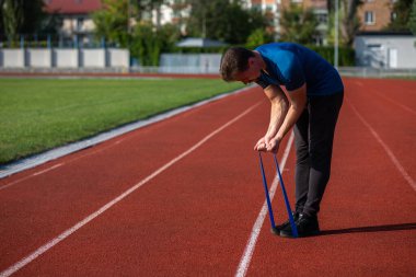 Sportif sakallı adam güneşli bir günde stadyumda elastik direniş bandıyla antrenman yapıyor. Boş boşluk