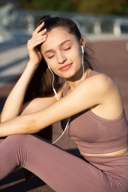 Genç atletik kadın dışarıda idmandan sonra dinleniyor ve kulaklıkla müzik dinliyor. Yakın çekim, spor konsepti