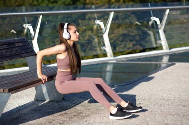 Uzun parlak saçlı genç atletik bir kadın köprüde egzersiz yapıyor ve müzik dinliyor. Metin için boşluk