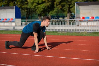 Atletik sakallı genç adam stadyumdaki koşu pistinde koşmaya hazır. Metin için boşluk