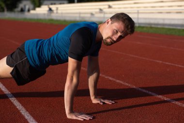Spor giyim içindeki kaslı adam stadyumda şınav çekiyor. Boş alan