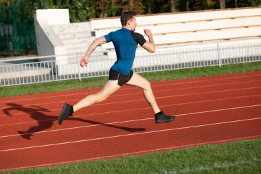 Genç koşucu güneşli bir akşamda stadyumda antrenman yapıyor. Metin için boşluk