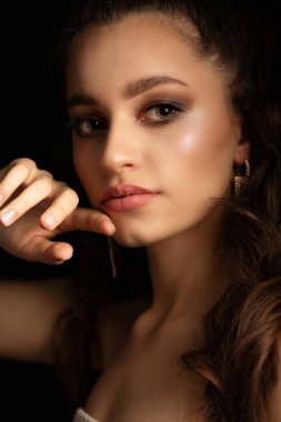 Koyu renk stüdyoda poz veren uzun gür saçlı şık esmer kadın.