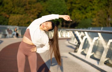 Uzun saçlı muhteşem bir koşucu kadın spor giysileri giyer ve antrenmandan önce ısınır. Boş boşluk