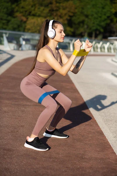 Sporty Woman Doing Squats Resistance Band Listening Music Earphones — Stock Photo, Image
