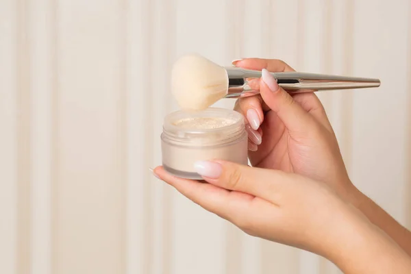 Woman using light mineral powder with a brush on a beige background. Empty space